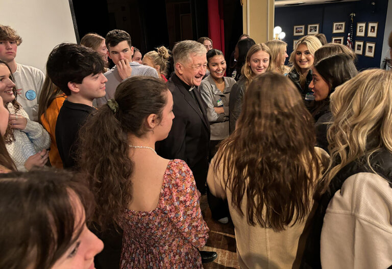 Cardinal Cupich grins as he stands in the middle of a group of over a dozen youth students, who eagerly greet him and talk about the environment.